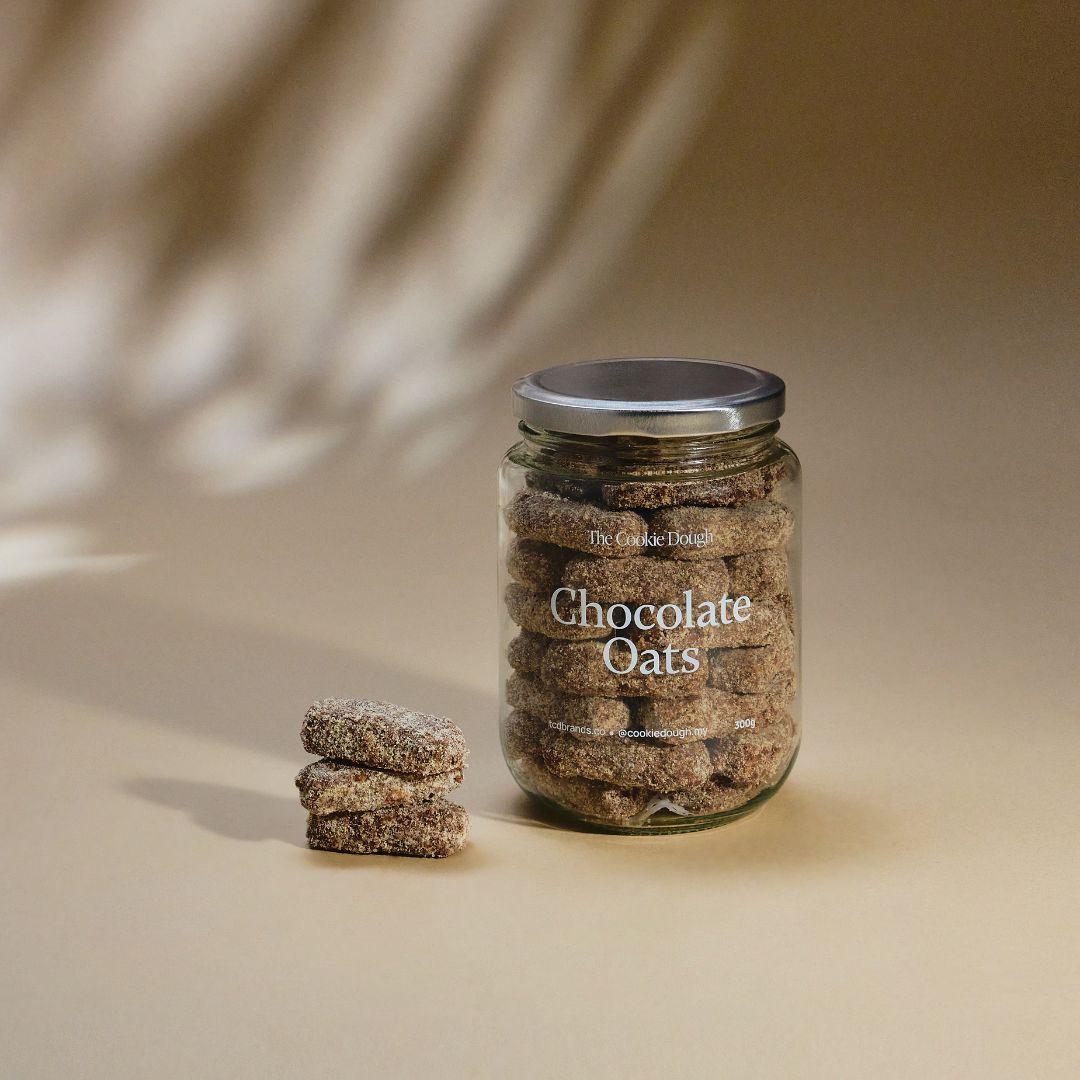 Jar of 'Chocolate Oats' cookies with a stack of cookies on a beige background
