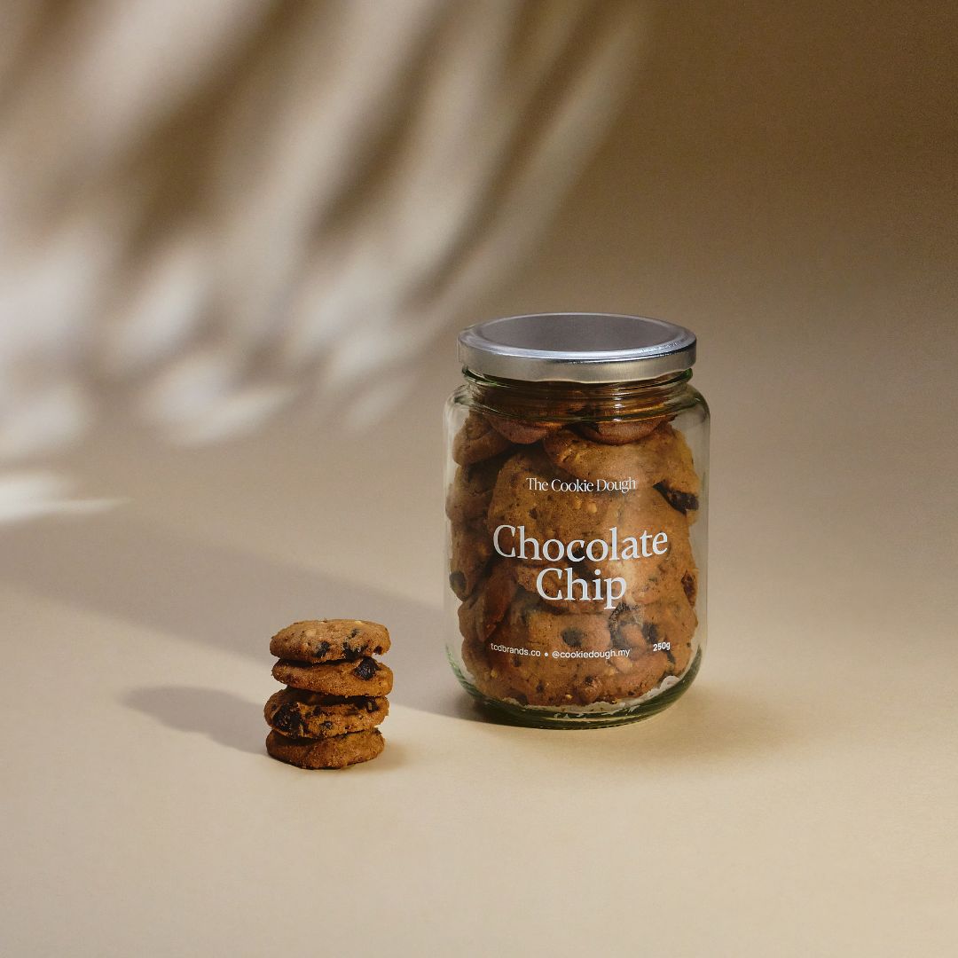 Jar of chocolate chip cookies with a stack of cookies on a beige background